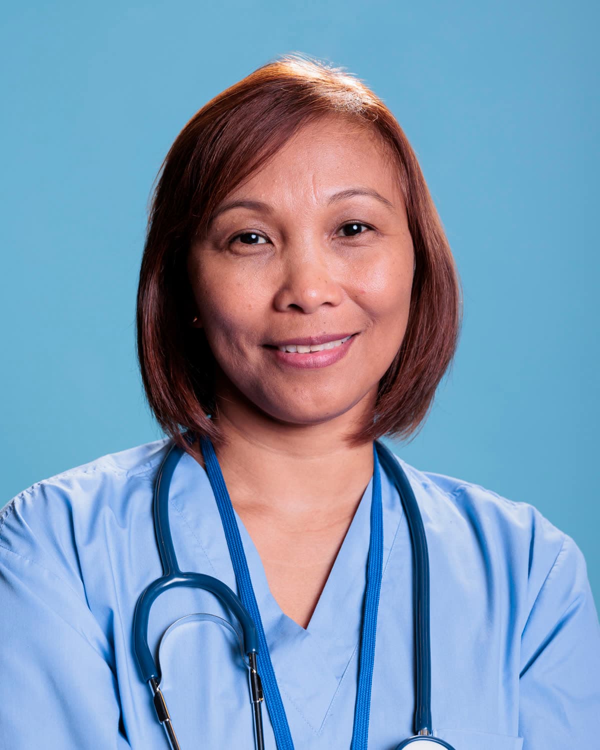 A smiling dentist in light blue scrubs with a stethoscope