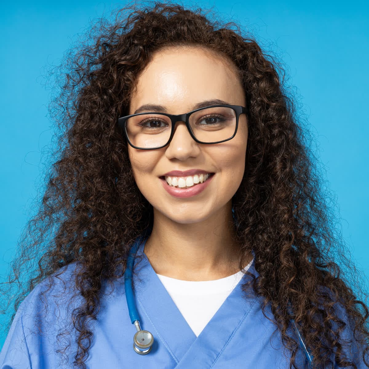 A smiling dentist with curly hair and glasses in blue scrubs