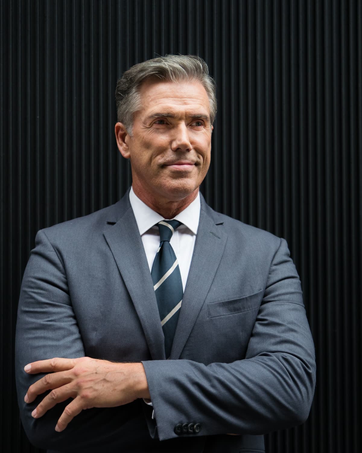 A broker in a gray suit and tie with his arms folded