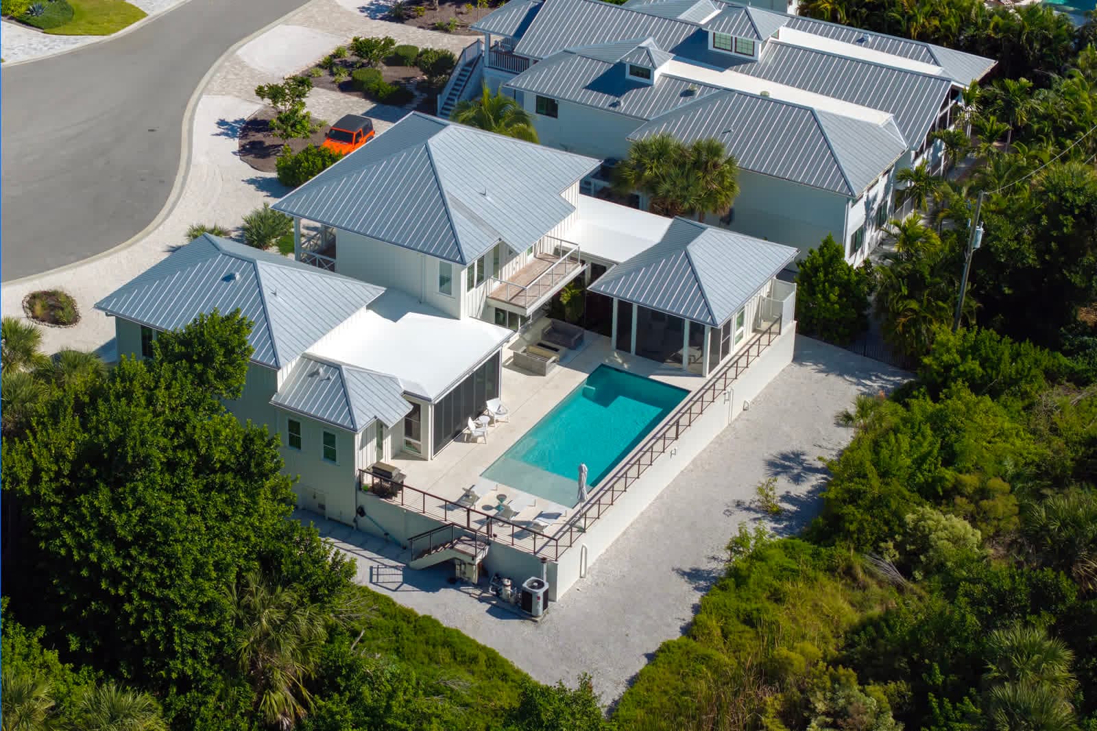 Aerial view of a white two-story home with a pool and a screened porch among trees
