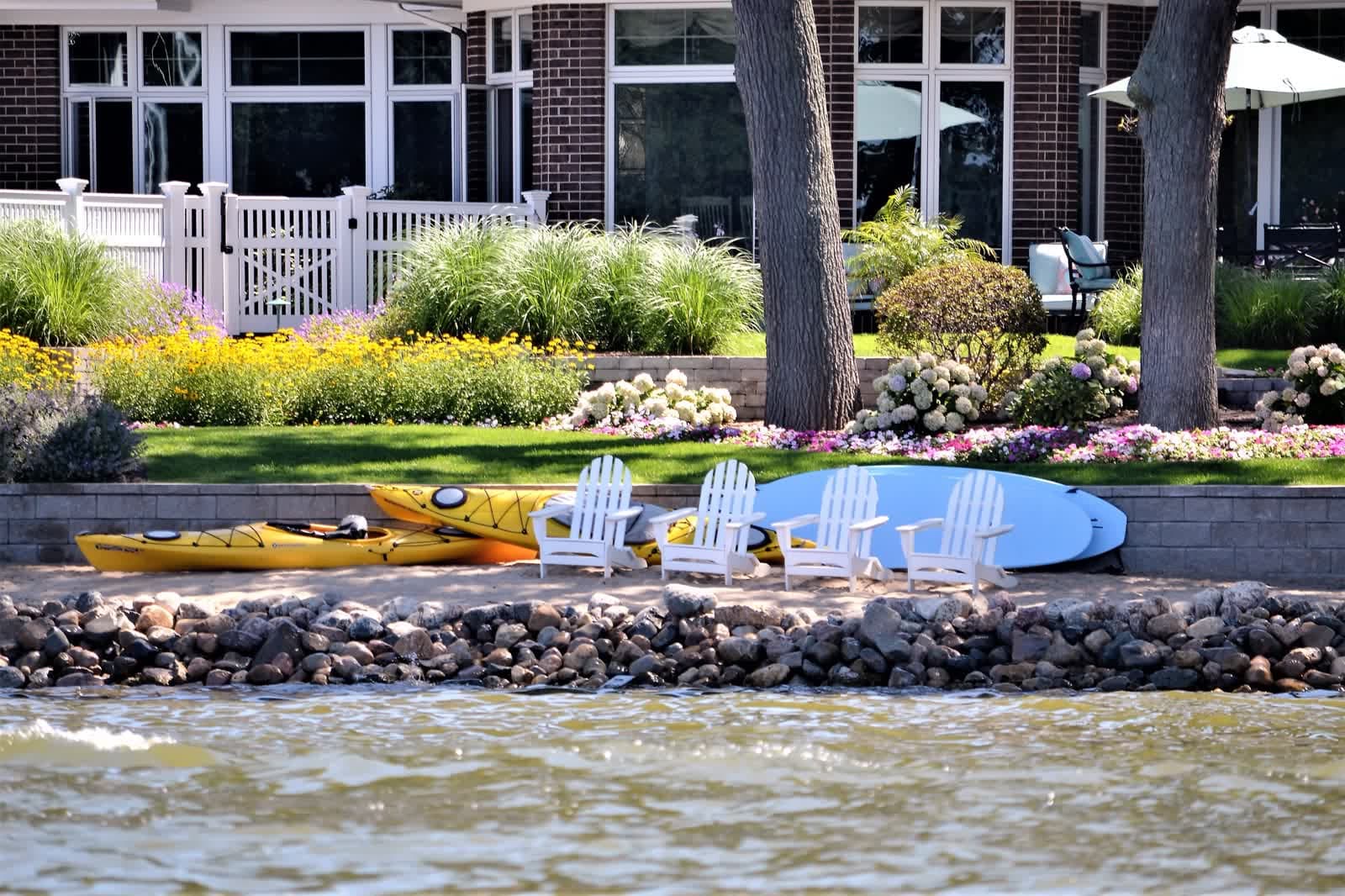A backyard garden with chairs and kayaks on the water's edge