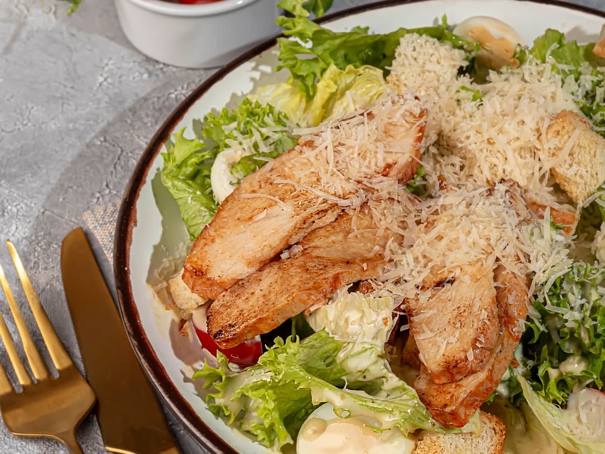 Caesar salad with sliced grilled chicken and shaved cheese