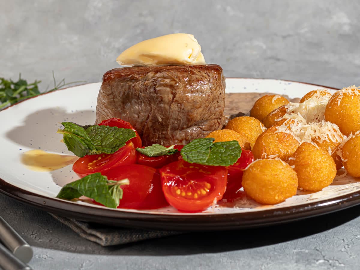 A thick steak with crispy potato balls and cherry tomatoes